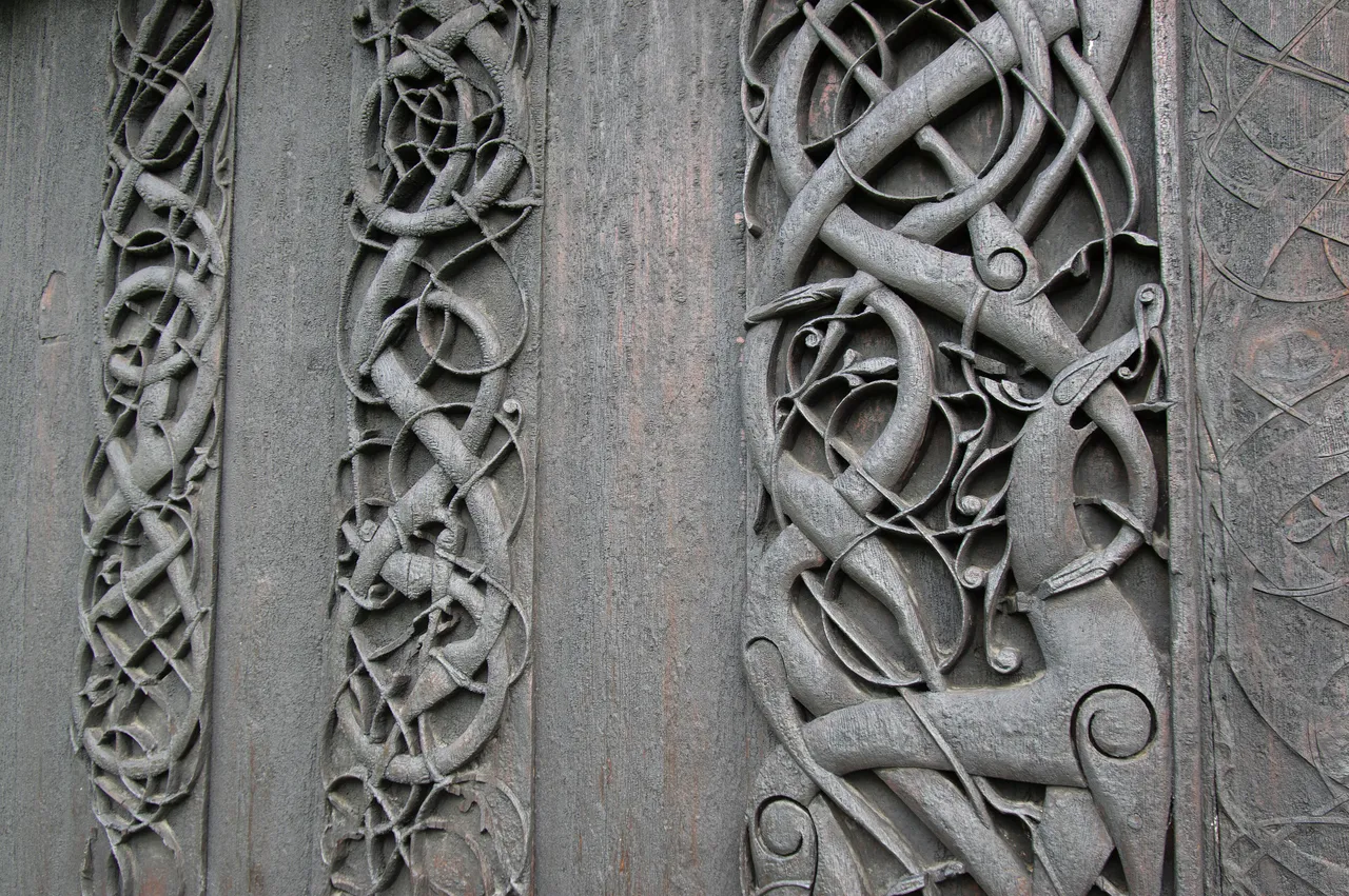 Close-up of dark weathered wooden planks carved in deep relief with long, slender interlaced animals and looping tendrils